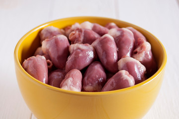 Raw chicken hearts in a yellow bowl on a white wooden table. Close-up.