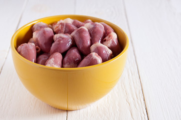 Raw chicken hearts in a yellow bowl on a white wooden table.