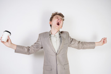 tired teen boy in grey business suit with paper Cup of coffee in hand on white studio background