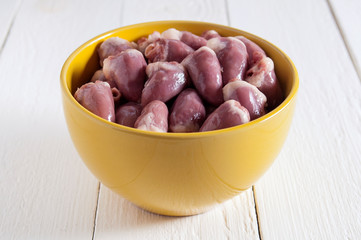 Raw chicken hearts in a yellow bowl on a white wooden table. In the center of the frame.