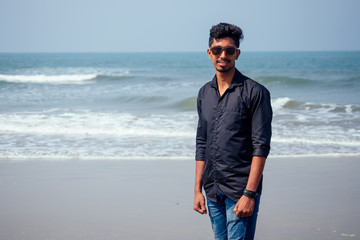 young hindu stylish man posing with sunglasses active beach vacation on semmertime happy Goa India beach. sunscreen spf protection concept.