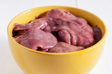 Raw chicken livers in a yellow bowl on a white wooden table. Close-up. Useful diet food.