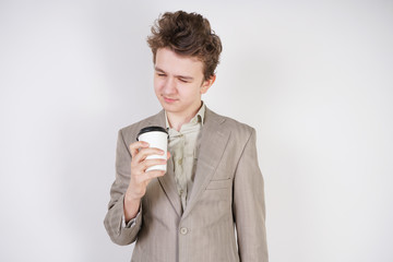 tired teen boy in grey business suit with paper Cup of coffee in hand on white studio background