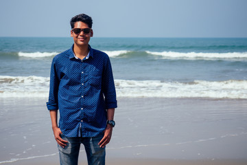young hindu stylish man posing with sunglasses active beach vacation on semmertime happy Goa India beach. sunscreen spf protection concept.