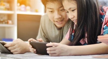 Asian boy and girl playing game on mobile phone together with smile face.