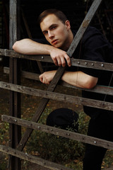 attractive guy on the street, in black, leaning on a hedge,fence