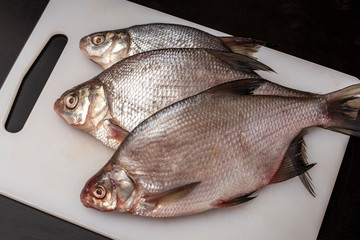 Fresh bream fish on a plastic cutting board, white. Dark background. Top view