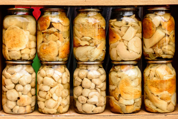 Delicious delicious white marinated mushrooms in glass jars on shelves.
