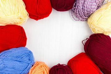 Flatlay of multicolored pastel knitting skeins of yarn and knitting needles on white background