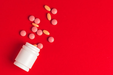 White pills spilling out of a toppled white bottle on red background