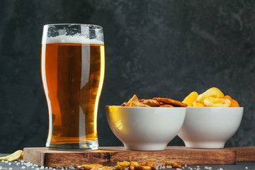Glass of lager beer with snack bowls on dark stone background