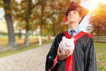 Happy young graduation man with piggy bank