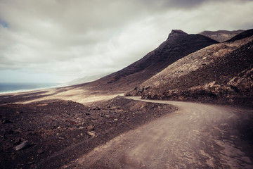 Off road adventure road in the mountains with beach view in wild scenic landscape for alternative travel vacation in the outdoors - cloudy dramatic sky for freedom holiday concept