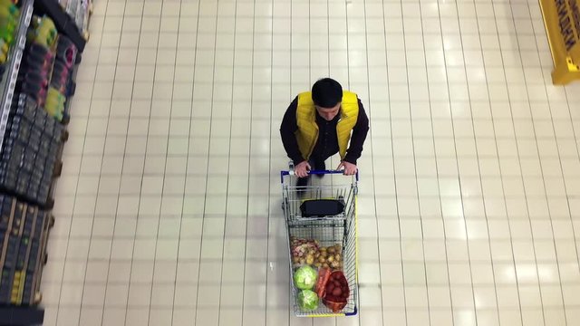 A Shopper Pushes A Trolley Along A Supermarket Aisle - View From The Top.