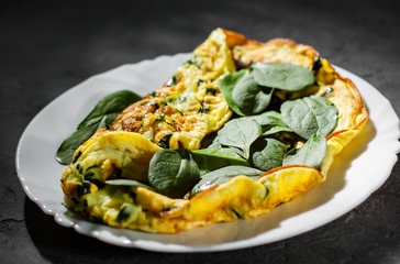 omelet with spinach in white plate on Dark grey black slate background