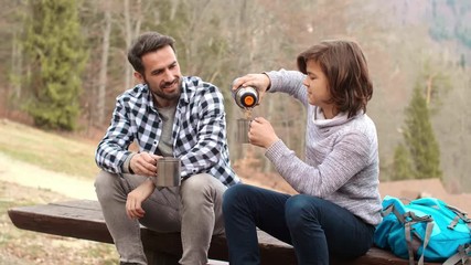 Happy boy and his dad drinking hot tea during hiking