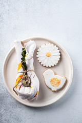 Table setting for the holiday of Easter. The photo shows white dishes, serving mat, Easter egg in a napkin. Napkin draped under rabbit ears.