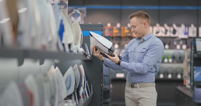 A young handsome man examines the iron in the store to buy a new apartment. evaluates the usability