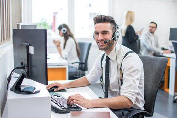 Smiling friendly customer support operator with headset working on computer in call center