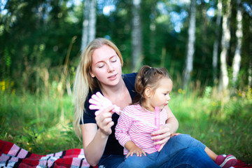 Mother and little daughter blowing soap bubbles outdoor. Parent and kid having fun in park. Happy and carefree childhood. Good family relations.