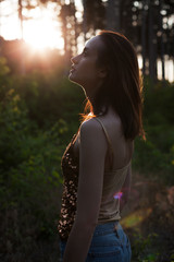 Beautiful young adult woman in forest at sunset.