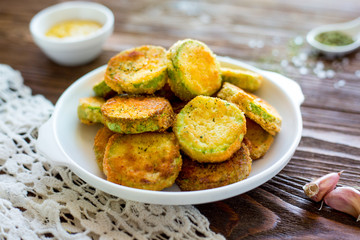 baked zucchini in breading and with parmesan.  garlic on a wooden table.  homemade dish.