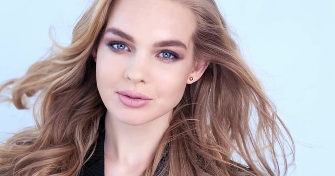 Beautiful young blonde woman with  long hair. Fashion model looks to the camera. Stunning face of a caucasian girl. Sexy model with a beautiful blue eyes. Slow motion. Beauty concept. 4k footage.