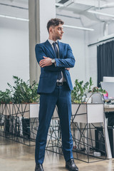 handsome, confident businessman standing in office with crossed arms and looking away