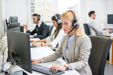 Female secretary with headphones and microphone solving client's problem while working on computer...
