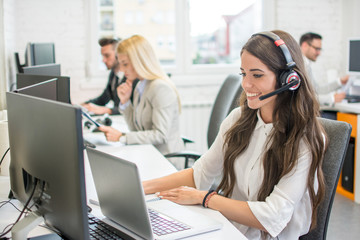 Beautiful young woman with headset using laptop while talking with client. Online customer support. - obrazy, fototapety, plakaty