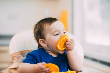 a little girl in a blue t-shirt and a blue plate sitting in a child's chair eating an orange