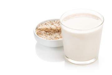 Glass of oat milk and grains in white bowl