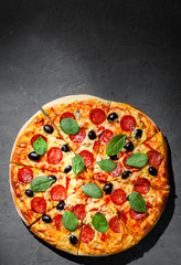 Pepperoni Pizza with Mozzarella cheese, salami, olive, pepper, Spices and Fresh spinach. Italian pizza on Dark grey black slate background