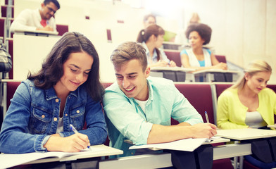 education, high school, university, learning and people concept - group of international students with notebooks writing at lecture hall