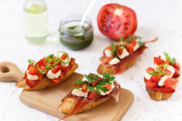 Italian appetizer - bruschetta with tomatoes, chili, sausage and cheese on a wooden board