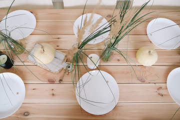 Holiday table decoration with white decorative pumpkins, white plates and candles on wooden background. Autumn composition. Autumn, fall, Halloween, Thanksgiving day concept. Flat lay, top view