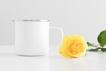 Enamel mug mockup with a yellow rose on a white table.