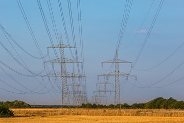 Hochspannungsleitung gespannt zwischen Strommasten bei strahlend blauem Himmel