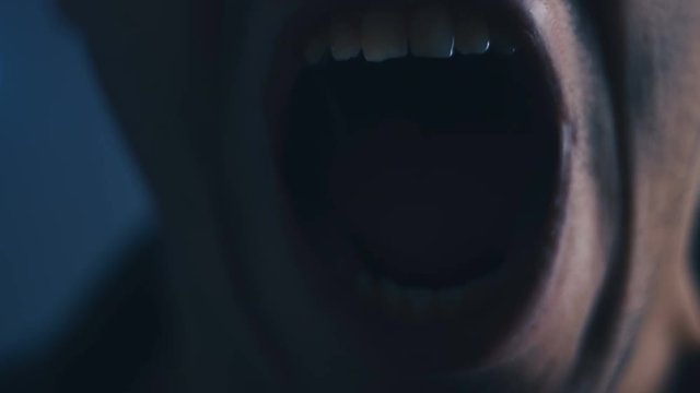 Aggressive Man with Angry facial expression Screaming out loud in dark. Close up of man Shouting with Mouth wide open.