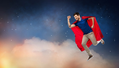 Fototapeta na wymiar super power and people concept - happy young man in red superhero cape flying in air over starry night sky background