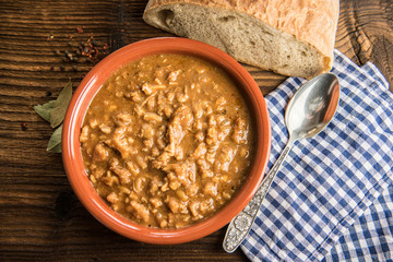 tripe stew sauce in brown ceramic pot on a wood table 