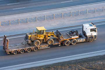 Truck with a long trailer platform for transporting heavy machinery, loaded tractor with a bucket....