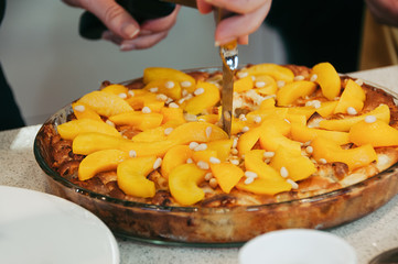 Delicious vegan peach cake decorated with pine nuts, whole, in round glass pan, on table. Selective...