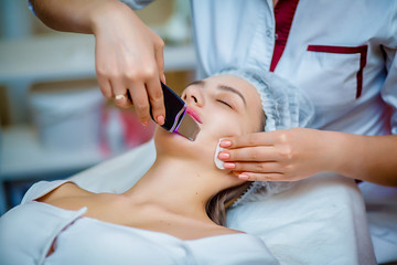 Woman receiving ultrasonic facial exfoliation at cosmetology salon. Procedure clearing clogged pores, ultrasonic treatment for skin rejuvenation, beautician uses modern apparatus for refreshing