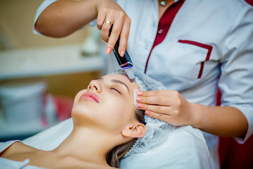 Woman receiving ultrasonic facial exfoliation at cosmetology salon. Procedure clearing clogged...
