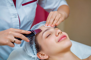 Woman receiving ultrasonic facial exfoliation at cosmetology salon. Procedure clearing clogged...