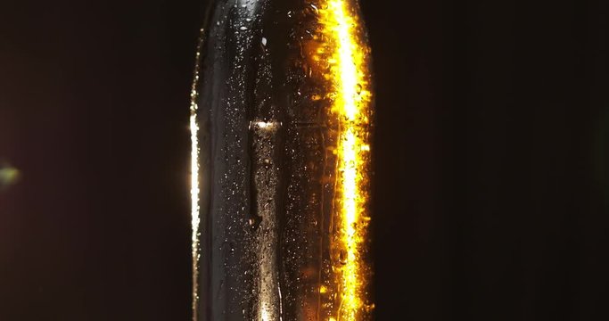 Bottle of cold beer on a black background. It slowly rotates. Condensate