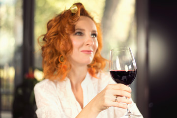 Portrait of a redhead girl in hair curlers with a glass of red wine