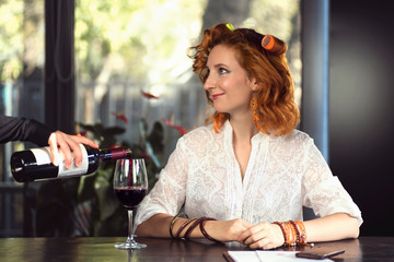 Red-haired girl in hair curlers in a cafe with a glass of wine