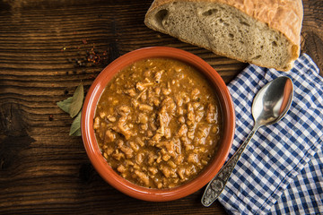 tripe stew sauce in brown ceramic pot on a wood table 